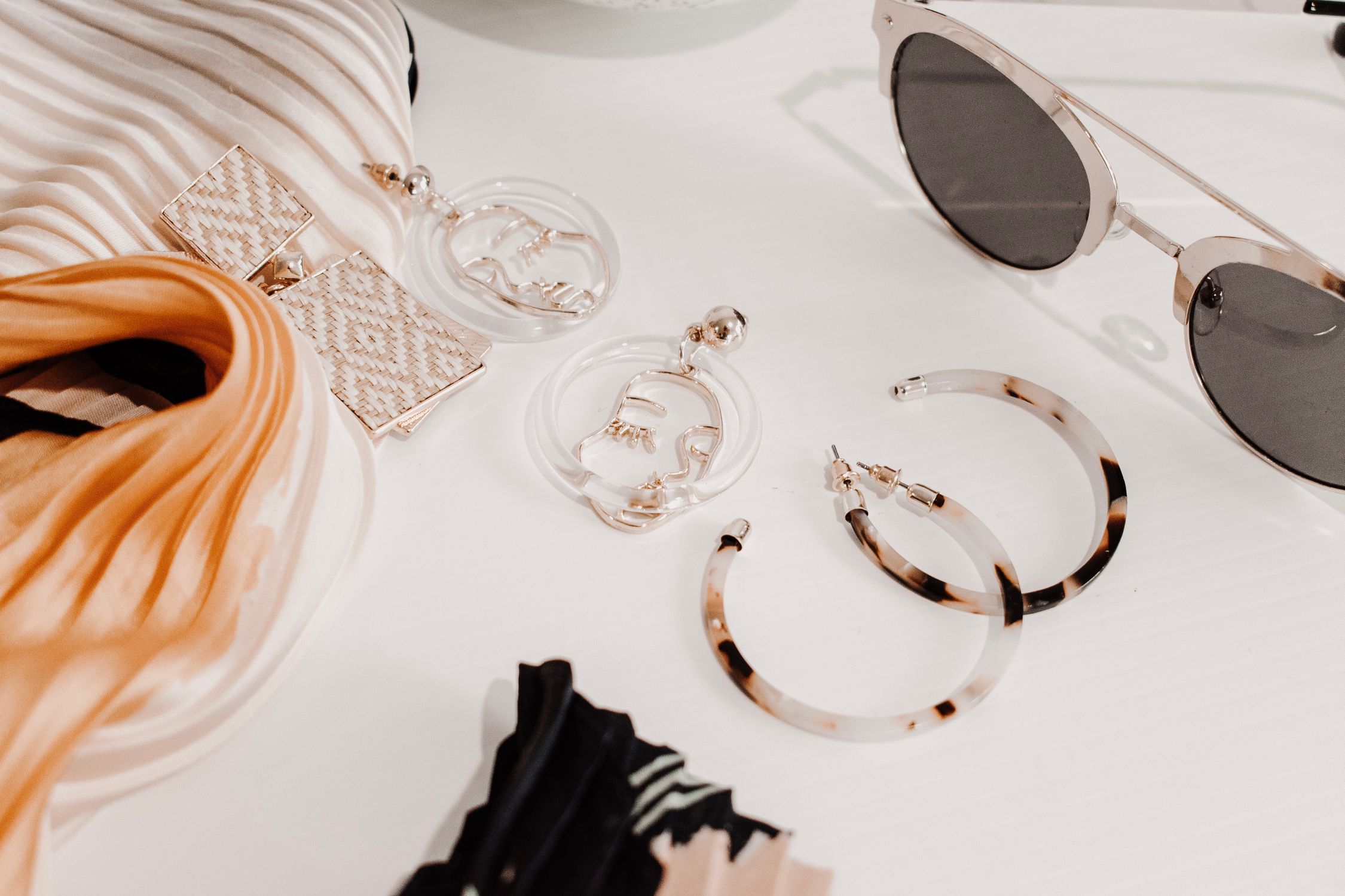 Earrings, sunglasses, and a silk scarf arranged on a light surface