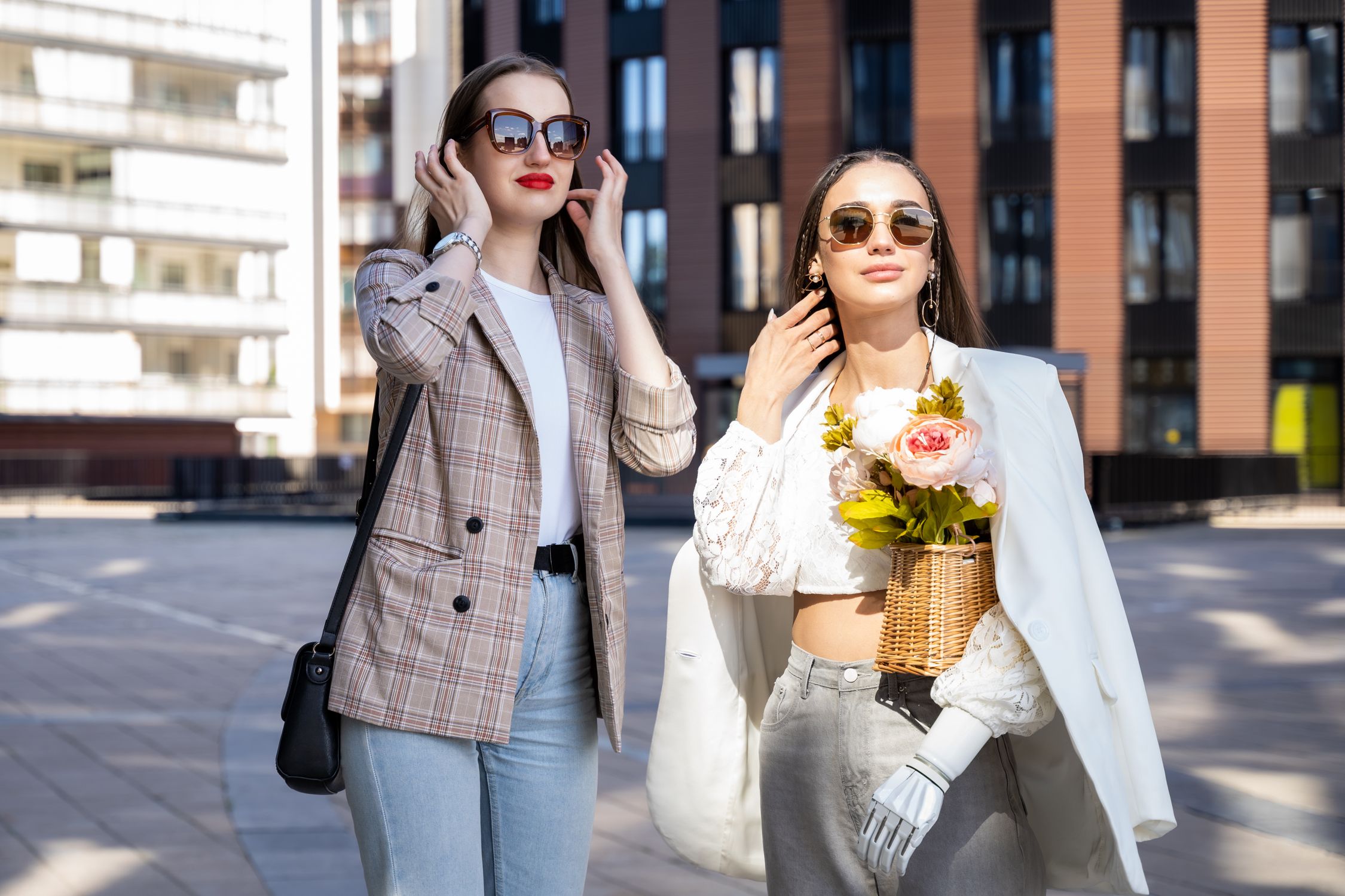 Two women in sunglasses and light tailoring on a city street